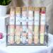 Assorted bath salts by Whole Self Aromatherapy in test tubes on elegant white linen, with a plant and pink flower in the background.